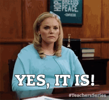 a woman in a blue shirt is sitting at a desk and says " yes it is "