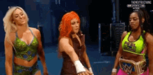 three female wrestlers are standing next to each other in a dark room .