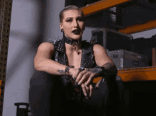 a woman wearing a choker and a leather vest sits in a warehouse