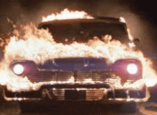 a car is on fire in a dark room with flames coming out of it .