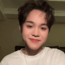 a young man wearing a white t-shirt and a necklace is smiling at the camera .