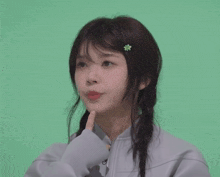 a girl with a braid and a teddy bear in her hair says hmm on a green background