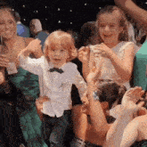 a little boy in a white shirt and bow tie is dancing in a crowd