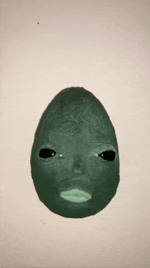 a green egg with a face on it is on a white background .