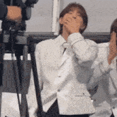 a man in a white suit is covering his mouth with his hand while standing in front of a tripod .