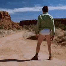 a man in diapers is standing on a dirt road in the desert .