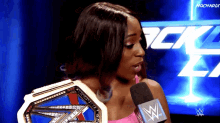 a woman is holding a wrestling championship belt and talking into a microphone with a wwe logo in the background
