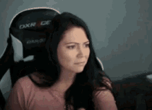 a woman is sitting in a gaming chair with a serious look on her face .