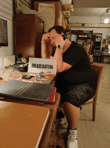 a man wearing headphones sits at a desk with a sign on it that says peaceeaatelb