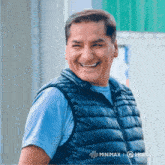 a man wearing a blue shirt and black vest is smiling