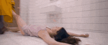 a woman is laying on her back in a bathroom with a yellow towel on her head