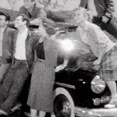 a black and white photo of a group of people standing around a car that says white car on the side