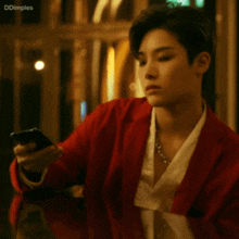 a man in a red jacket is looking at a cell phone with ddimples written below him