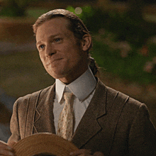 a man in a suit and tie holds a straw hat in his hands