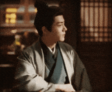 a man with a bun on his head is sitting at a table in front of a window