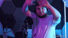 a man wearing headphones stands in front of a microphone with gifrun.com written on the bottom right