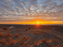 a person standing on top of a sand dune watching the sun set