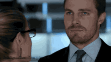 a man in a suit and tie looks at a woman in glasses behind a tumblr post