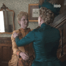 two women are hugging in a room with a hbo logo on the bottom left