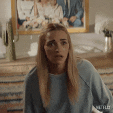 a woman in a blue sweatshirt is standing in front of a framed picture of a family .