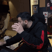 a man wearing a black and red hoodie is sitting in a chair