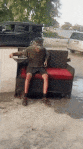 a man sits on a couch in a driveway with a van in the background