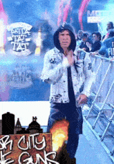 a man in a hooded jacket stands in front of a sign that says city of guns
