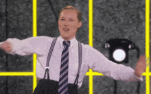 a woman wearing suspenders and a tie stands in front of a phone