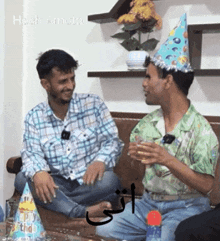 two men wearing party hats are sitting on a couch and one of them is wearing a birthday hat