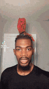 a man with a beard is wearing a black shirt and a red object on his head .