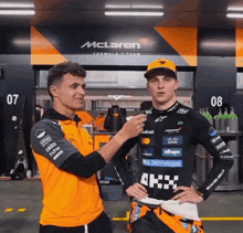 two men are standing in front of a mclaren formula 1 team sign