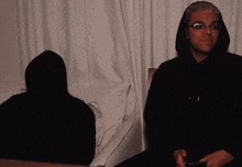a man in a hooded sweatshirt sits next to another man in a black hoodie