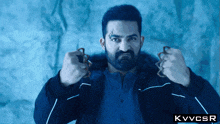 a man with a beard is holding a pair of scissors in front of a blue background that says kvvcsr