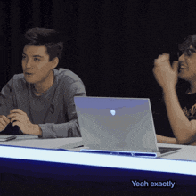 two men sitting at a table with a laptop and yeah exactly written on the bottom