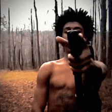 a shirtless man is pointing a gun at the camera in a forest