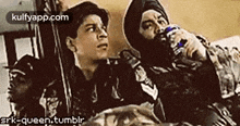 a man in a turban is holding a bottle of water while another man looks on .