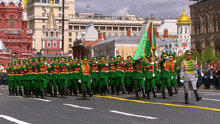a group of soldiers marching down a street with a green flag in the foreground