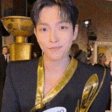 a man wearing a black jacket and a gold ribbon around his neck is holding a trophy .