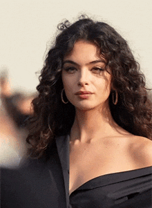 a woman with curly hair and hoop earrings is wearing a black off the shoulder top .