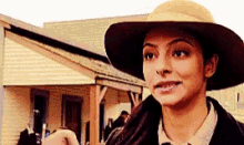a woman wearing a hat and a jacket is standing in front of a house .