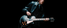 a man in a leather jacket is playing a guitar in a dark room