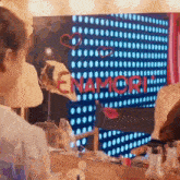 a woman is looking at herself in a mirror in front of a large screen that says enamori