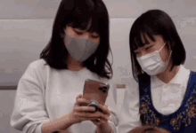 two girls wearing masks look at a cell phone