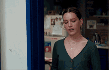 a woman in a green sweater is standing in front of a door