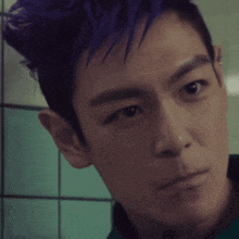 a man with purple hair looks at the camera with a serious look on his face