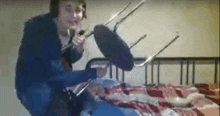 a man is sitting on a bed holding a chair up in the air .