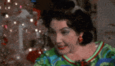 a woman in a green shirt and red earrings is smiling in front of a christmas tree