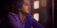 a young man in a denim jacket is sitting in a dark room looking up .