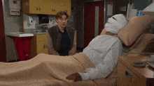 a man sitting next to a man in a hospital bed with a bandaged head