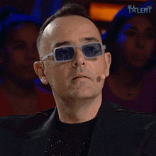 a man wearing sunglasses and a suit stands in front of a microphone that says talent